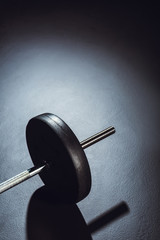 partial view of barbell on floor with shadow at gym