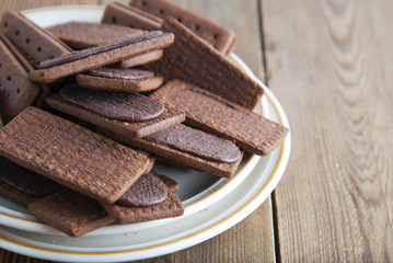 Chocolate cookies or biscuits and cream in, on wooden background. Close up sweet unhealthy snack or kids or adults.