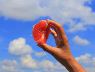 Beauty of nature, women and healthy eating.
The woman's hands hold a grapefruit against the sky and clouds. A close-up photo.