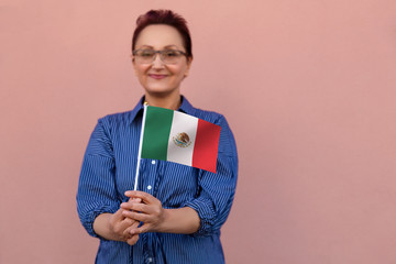 Mexico flag. Woman holding Mexican flag. Nice portrait of middle aged lady 40 50 years old with a national flag over pink wall background on the street outdoors.