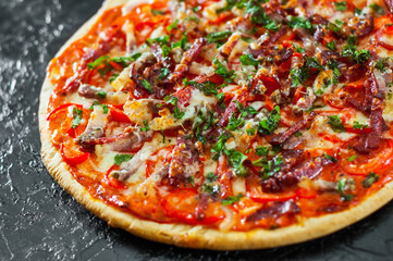 Pizza with Mozzarella cheese, Ham, Tomatoes, salami, pepper, bacon, pepperoni, Spices and Fresh Basil. Italian pizza on black background