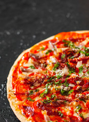 Pizza with Mozzarella cheese, Ham, Tomatoes, salami, pepper, bacon, pepperoni, Spices and Fresh Basil. Italian pizza on black background