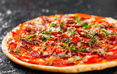 Pizza with Mozzarella cheese, Ham, Tomatoes, salami, pepper, bacon, pepperoni, Spices and Fresh Basil. Italian pizza on black background