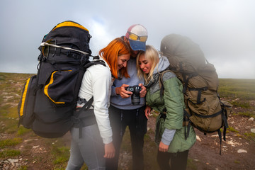 Travel Lifestyle and survival concept rear view. Hiking man and women with backpack enjoys a hike  and looks at the pictures taken on  camera in the mountains in the background a green floor and cloud