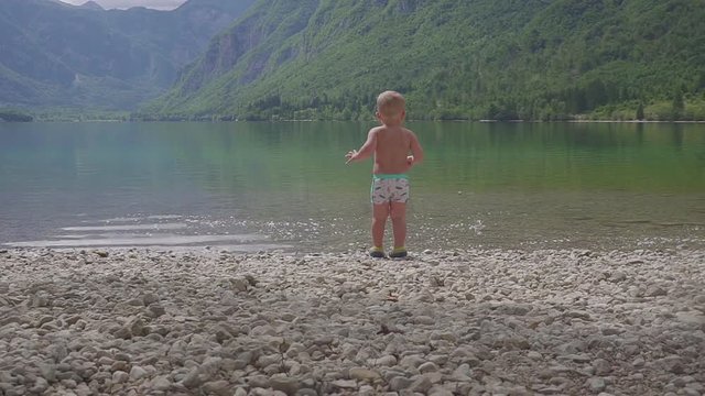 Little boy 2 years in the water of forest mountain lake. View from the back.