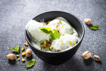 Pistachios ice cream in bowl on black stone table.