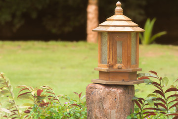 rustic wooden lantern placed on a wooden post in a lush garden, creating a warm and peaceful atmosphere. Ideal for landscaping, outdoor decor, and nature-themed content.