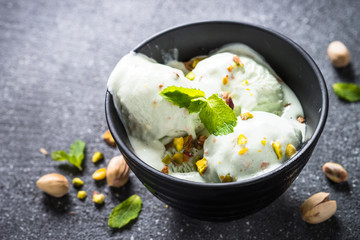 Pistachios ice cream in bowl on black stone table.