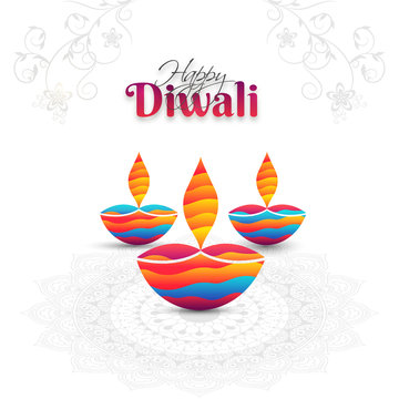 Illuminated colorful oil lamps (Diya) on floral mandala decorated white background for Diwali festival celebration. Can be used as greeting card design.