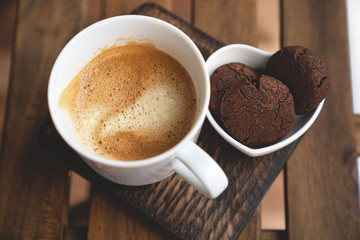 Chocolate cookies with dark chocolate and cup of coffee on a wooden background.