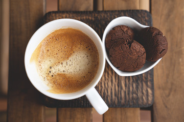 Chocolate cookies with dark chocolate and cup of coffee on a wooden background.