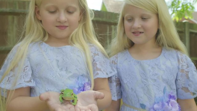Pre teen caucasian girl holding a white lipped tree frog beside her twin sister in her hands themes of imagination fantasy magic stories childhood