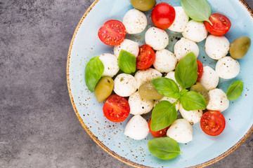 Delicious caprese salad with ripe cherry tomatoes and mini mozzarella cheese balls with fresh basil leaves.