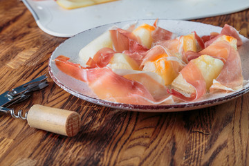 Prosciutto with melon on a plate. Preparation of cold snacks to red wine.