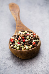 Peppercorn mix in a wooden bowl on grey table.
