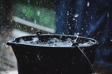 Rainy weather on the terrace in summer. The rain falls into the bucket and creates splashes.