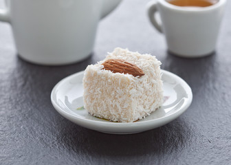Turkish delight with almonds in coconut chips on a saucer on a slate background.