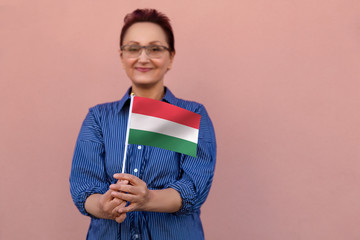 Hungary flag. Woman holding Hungarian flag. Nice portrait of middle aged lady 40 50 years old with a national flag of Hungary over pink wall background.