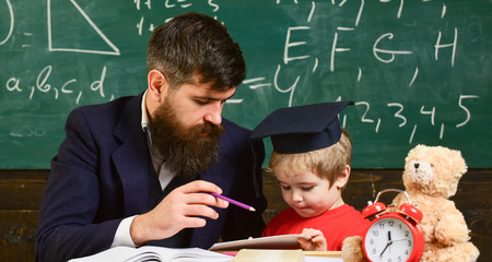 Male kindergarten teacher drawing picture with child. Teacher and pupil in mortarboard, chalkboard...