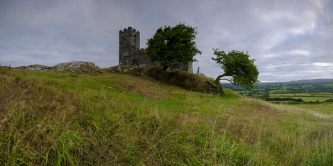 Summer sunrise on Brentor showning St Michael's church atop the tor with dramatic weather clouds of showers and mist, on the western edge of the Dartmoor National Park. UK