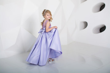 Fototapeta na wymiar Beautiful girl in long dress smiles. A child in a white room. Elegant dress on the girl