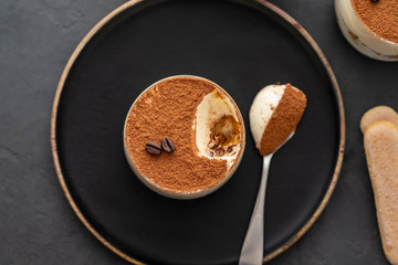 Delicious Italian dessert tiramisu, chocolate, cocoa and coffee beans on a black background. Top view with copy space.