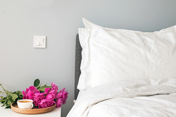 Bed with white bed sheets and pink peonies and coffee on the nightstand.