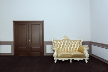 A classic sofa with gold leather upholstery against a light wall and a brown door. 