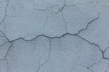 Old plastered wall of the house with large cracks in different directions
