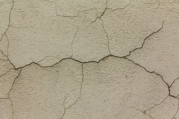Old plastered wall of the house with large cracks in different directions