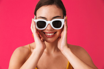 Fototapeta premium Photo closeup of european cheerful woman 20s wearing fashion earrings and glasses smiling at you, isolated over pink background