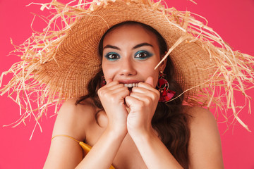 Image closeup of caucasian excited woman 20s wearing big straw hat biting fists in delight, isolated over pink background