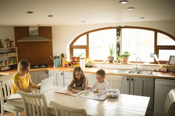 Children studying while mother working on laptop at home