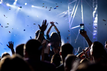 cheering crowd with raised hands and falling confetti at concert - music festival