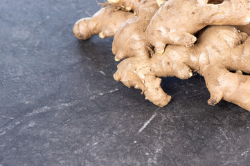 Whole ginger roots on dark old stone background table, space for text.