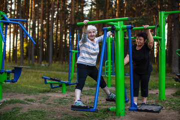 An elderly woman with an adult daughter is doing exercises on the sport playground in the Park.