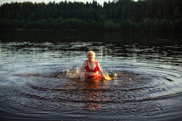 Elderly woman swimming in the summer river at sunset.