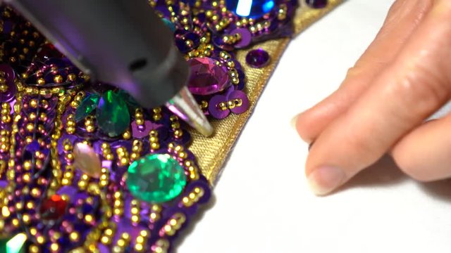 Extreme closeup of woman&rsquo;s finger pressing acrylic rhinestones into place with a glue gun.