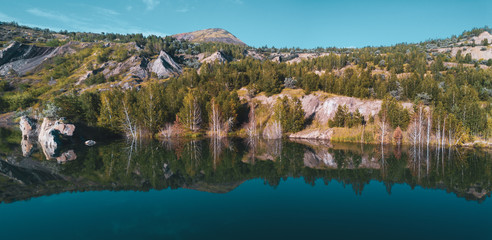 Aerial drone photo of beautiful shore reflecting in water,view inside abandoned quarry, the slopes overgrown of mixed forest, Russia