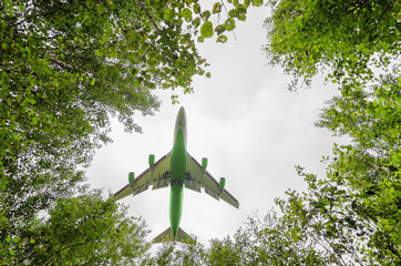 big green passenger aircraft delivers passengers and cargo, lands in the airport, wide view of owerflying above in a hole between forest trees in front of the cloudy sky background