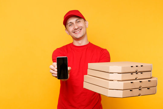 Delivery man in red cap t-shirt giving food order italian pizza in flatbox boxes on yellow background. Male employee pizzaman courier hold mobile phone with blank empty screen mockup. Service concept.
