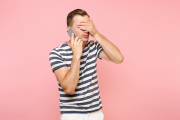 Portrait of sad upset young man talking on mobile phone, conducting pleasant conversation isolated on trending pastel pink background. People sincere emotions lifestyle concept. Advertising area.