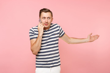 Fototapeta premium Portrait of fun emotional young man talking on mobile phone, conducting pleasant conversation isolated on trending pastel pink background. People sincere emotions lifestyle concept. Advertising area.