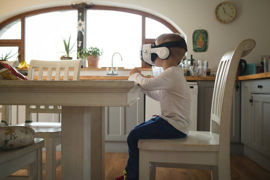 Side view of boy using virtual reality headset while sitting in kitchen
