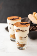 Homemade tiramisu, traditional Italian dessert in glass on white table. Copy space.