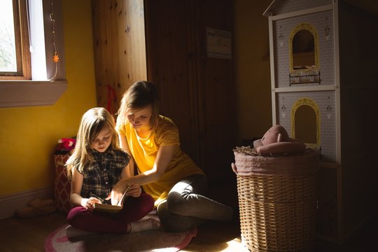 Daughter with mother reading a book in bedroom