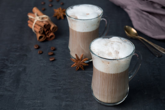 Coffee with rich milk foam in a glass beaker on a dark background sticks of cinnamon and stars of anise. Copy space