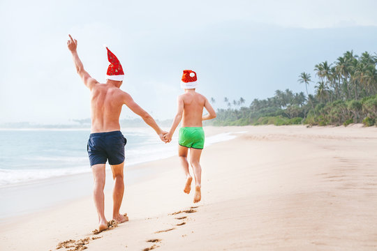Father and son in Santa's hats run on perfect sand beach on tropical island. Christamas and New Year holiday vacation