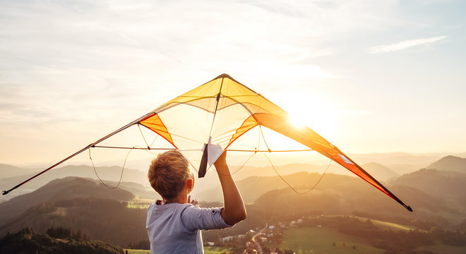 Boy starts to fly a kite over the mountain hills at sunset time