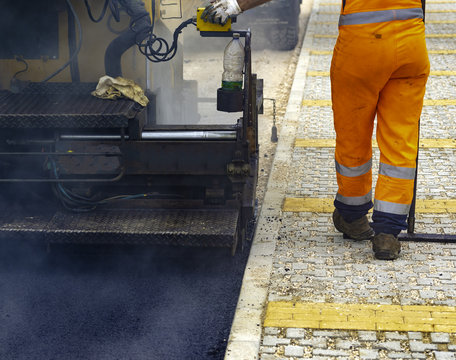 Workers regulate tracked paver laying asphalt heated to temperatures above 160 ° pavement on a runway